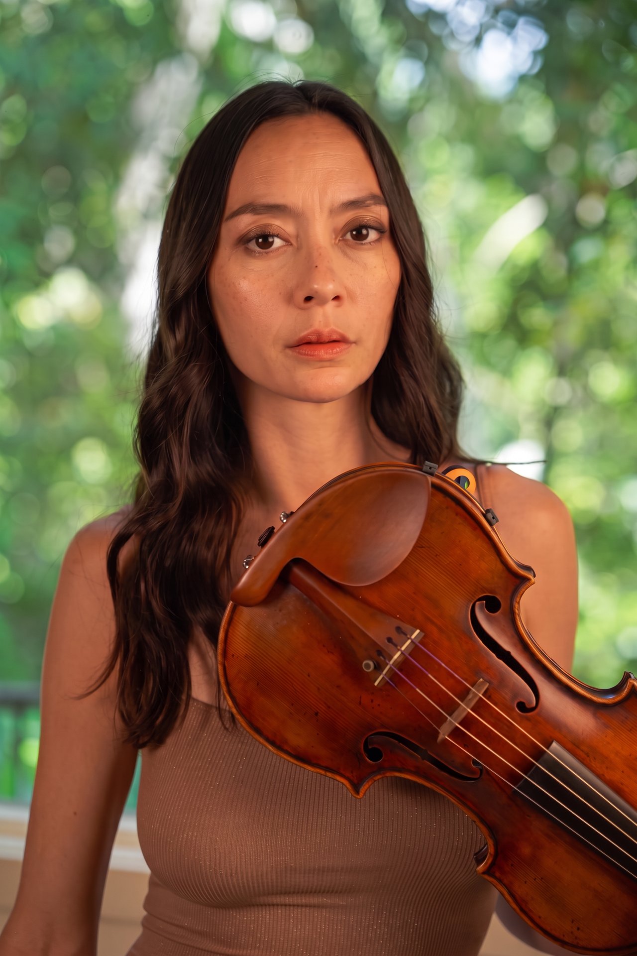Lucia Micarelli holding her violin at her chest in a garden